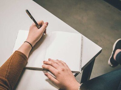 Hands writing in a notebook – Creative Nonfiction writing workshop